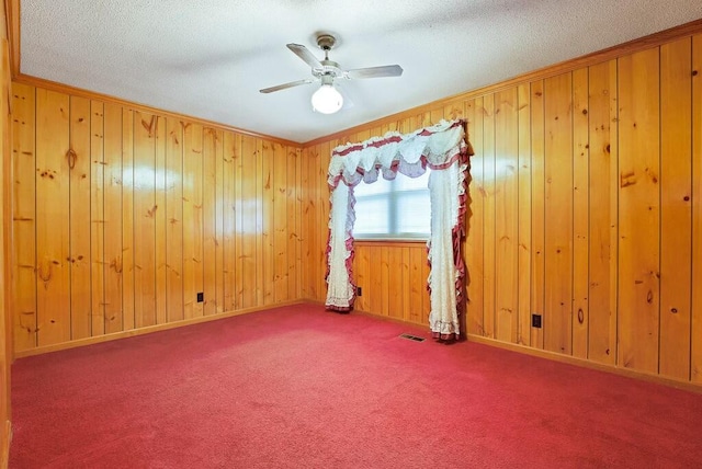 spare room with carpet, a textured ceiling, and wooden walls