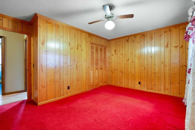 spare room with ceiling fan, a textured ceiling, wooden walls, carpet, and ornamental molding