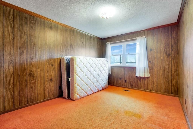 spare room with light carpet, wood walls, a textured ceiling, and ornamental molding