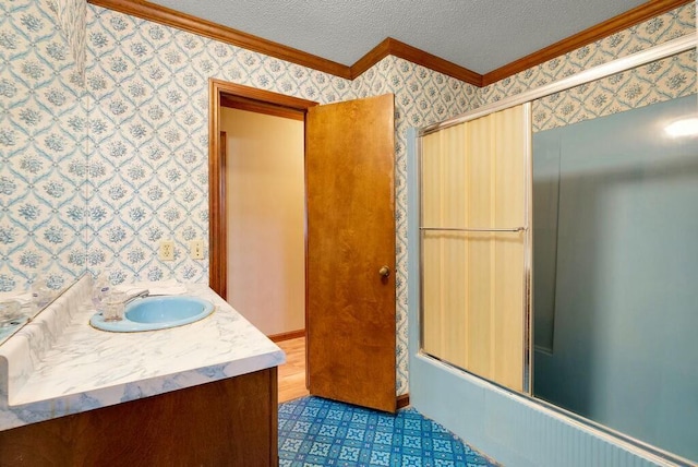 bathroom with a textured ceiling, vanity, ornamental molding, and bath / shower combo with glass door