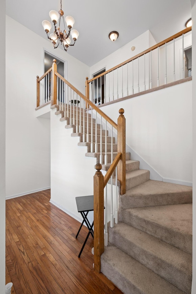 stairs with hardwood / wood-style floors and a chandelier