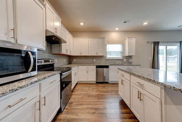 kitchen with white cabinetry, stainless steel appliances, light stone counters, backsplash, and light wood-type flooring