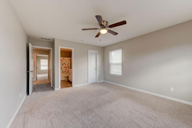 unfurnished bedroom featuring a closet, light colored carpet, ensuite bath, and ceiling fan