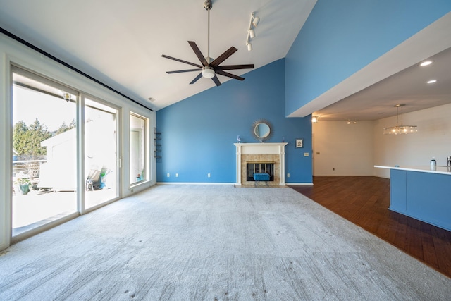 unfurnished living room with lofted ceiling, a high end fireplace, ceiling fan with notable chandelier, and hardwood / wood-style flooring