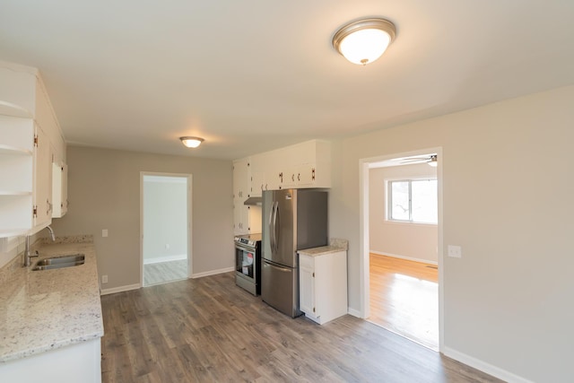 kitchen featuring sink, appliances with stainless steel finishes, white cabinetry, hardwood / wood-style floors, and light stone counters