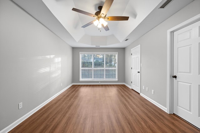 unfurnished room featuring a raised ceiling, ceiling fan, and dark hardwood / wood-style floors