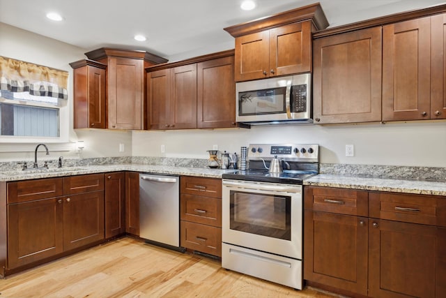 kitchen featuring light stone countertops, sink, light wood-type flooring, and appliances with stainless steel finishes