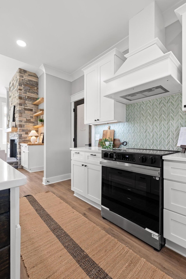 kitchen with white cabinets, decorative backsplash, stainless steel stove, and custom range hood