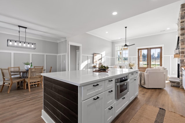 kitchen featuring a center island, oven, crown molding, decorative light fixtures, and white cabinetry