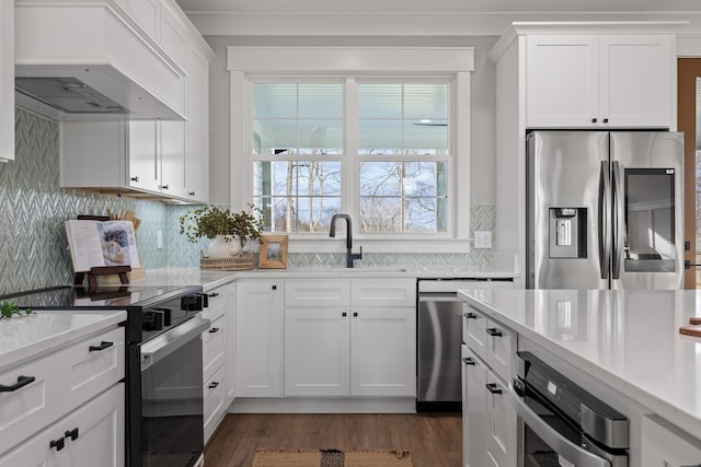 kitchen featuring custom exhaust hood, white cabinetry, sink, and appliances with stainless steel finishes