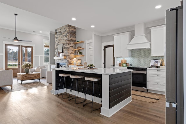 kitchen with a center island, premium range hood, stainless steel range oven, white cabinetry, and a breakfast bar area