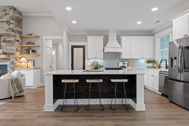 kitchen featuring appliances with stainless steel finishes, white cabinetry, a kitchen island, and custom exhaust hood