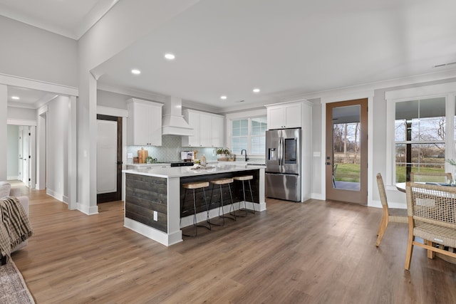 kitchen featuring a center island, backsplash, stainless steel fridge, white cabinets, and custom exhaust hood