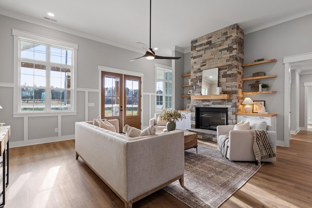 living room with hardwood / wood-style flooring, ceiling fan, a stone fireplace, and crown molding