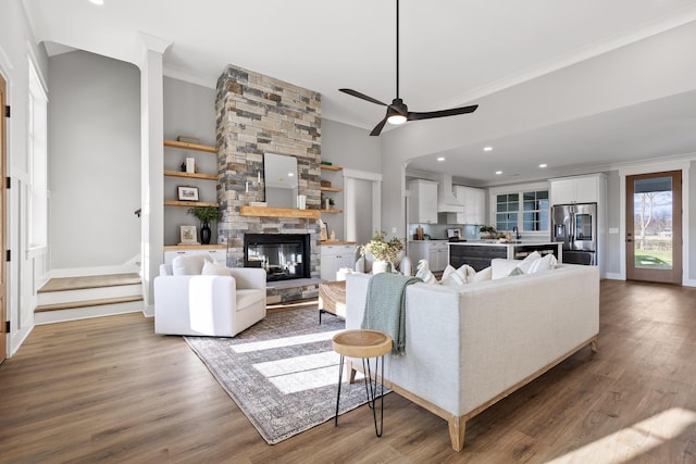 living room featuring dark wood-type flooring, a stone fireplace, sink, ceiling fan, and ornamental molding