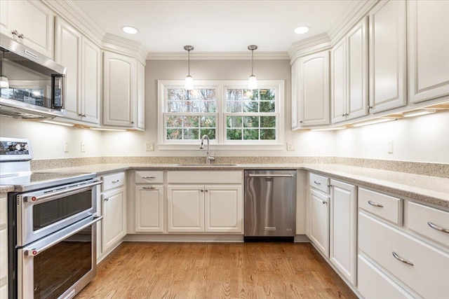 kitchen with sink, light hardwood / wood-style floors, decorative light fixtures, white cabinets, and appliances with stainless steel finishes