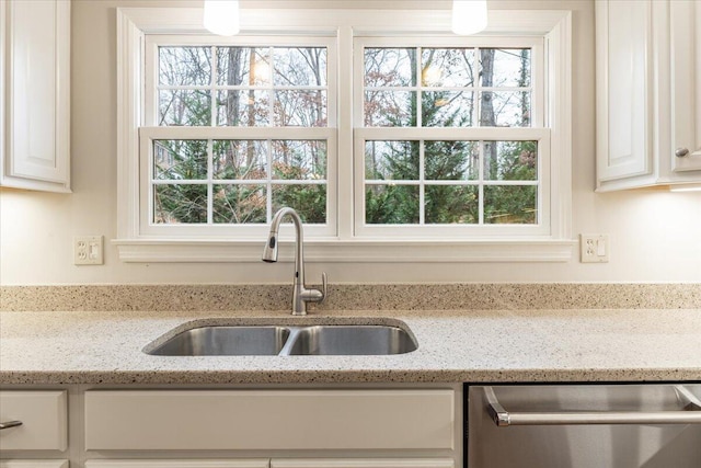 kitchen with stainless steel dishwasher, light stone counters, white cabinetry, and sink