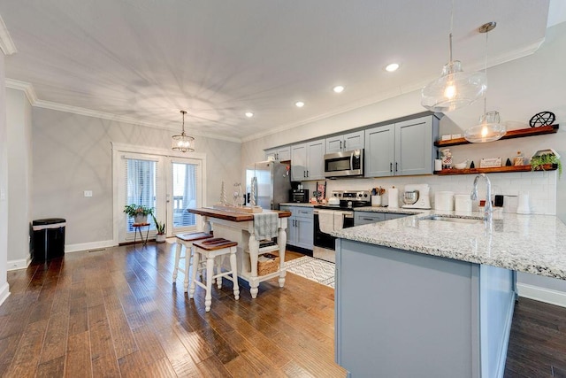 kitchen with kitchen peninsula, a kitchen bar, light stone counters, stainless steel appliances, and pendant lighting