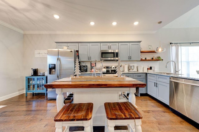 kitchen featuring light stone countertops, appliances with stainless steel finishes, sink, pendant lighting, and light hardwood / wood-style flooring