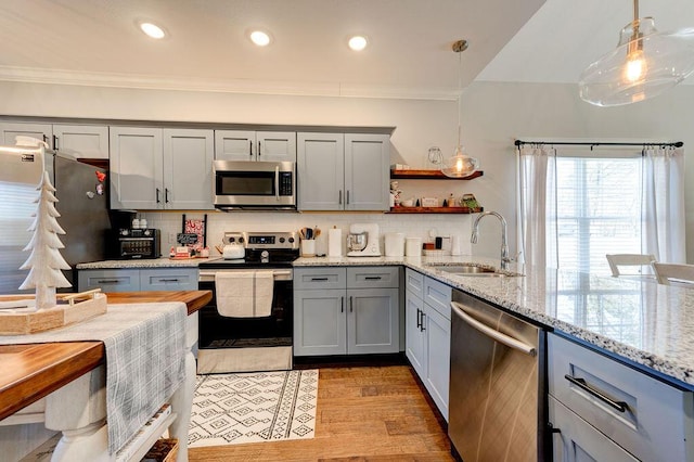 kitchen with backsplash, hanging light fixtures, light hardwood / wood-style flooring, appliances with stainless steel finishes, and light stone counters