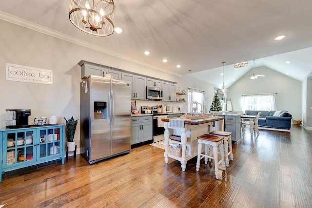 kitchen featuring gray cabinetry, ceiling fan with notable chandelier, stainless steel appliances, pendant lighting, and lofted ceiling