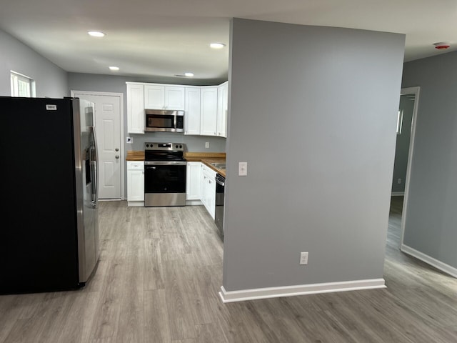 kitchen with white cabinets, wooden counters, stainless steel appliances, and light hardwood / wood-style floors