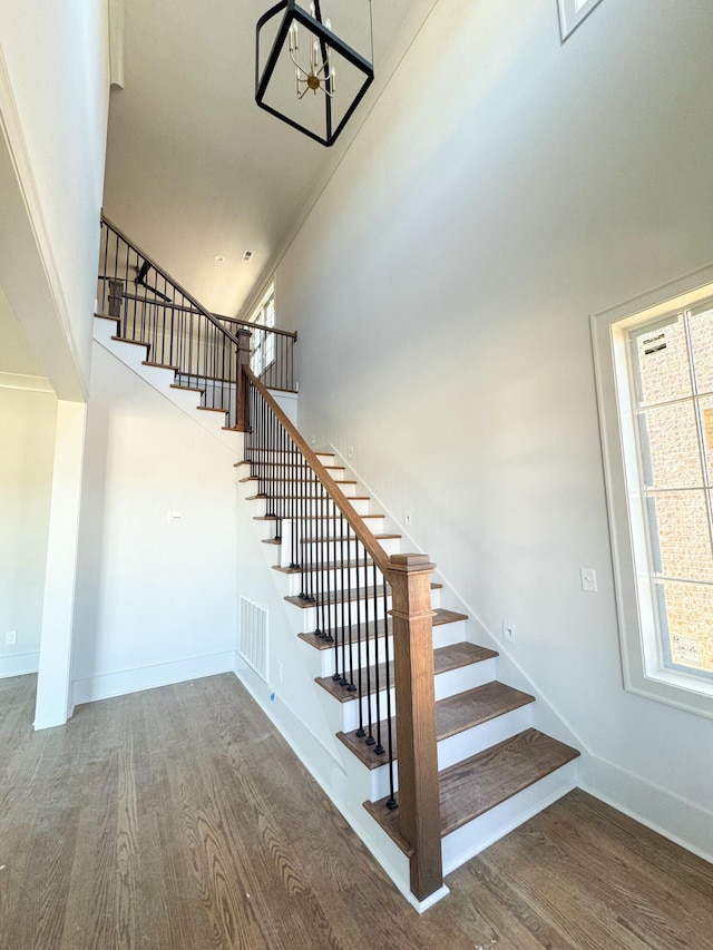 stairway featuring a towering ceiling, hardwood / wood-style flooring, and an inviting chandelier