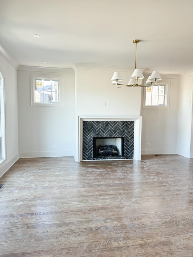 unfurnished living room featuring light hardwood / wood-style floors, an inviting chandelier, ornamental molding, and a tiled fireplace