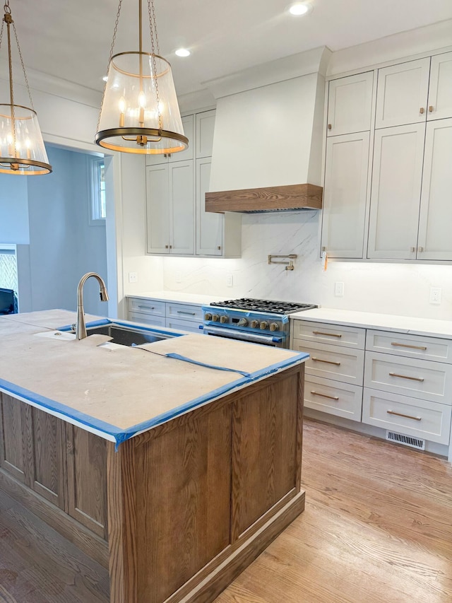 kitchen with a center island with sink, pendant lighting, sink, and premium range hood