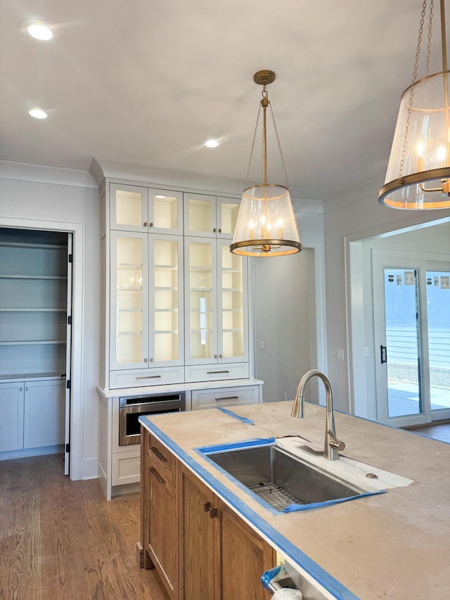 kitchen featuring ornamental molding, dark wood-type flooring, sink, white cabinetry, and hanging light fixtures