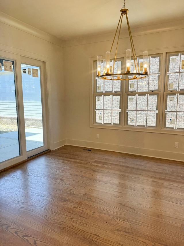 unfurnished dining area featuring ornamental molding, wood-type flooring, and a notable chandelier