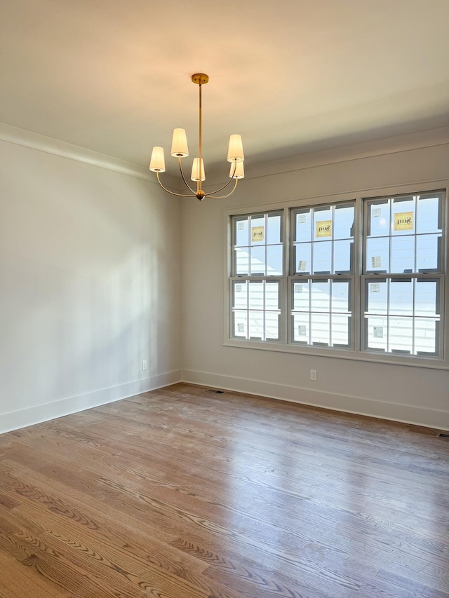 spare room with a chandelier, wood-type flooring, and crown molding