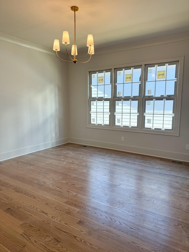 spare room featuring crown molding, dark wood-type flooring, and an inviting chandelier