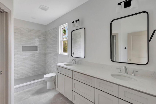 bathroom with a tile shower, tile patterned flooring, vanity, and toilet