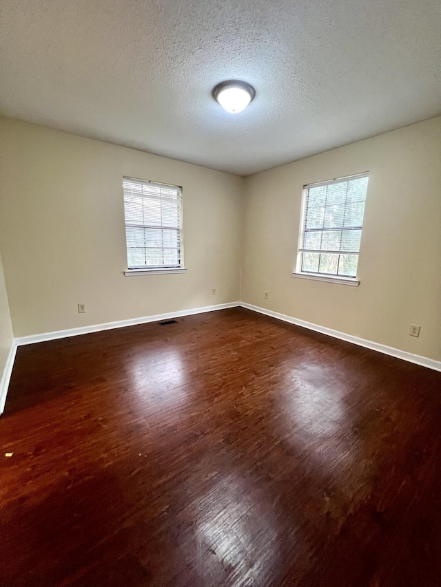 empty room with dark wood-type flooring and a textured ceiling