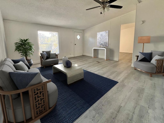 living room with ceiling fan, light wood-type flooring, and a textured ceiling