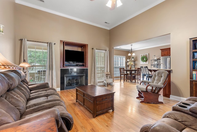 living room with ceiling fan with notable chandelier, ornamental molding, a tile fireplace, and light hardwood / wood-style flooring