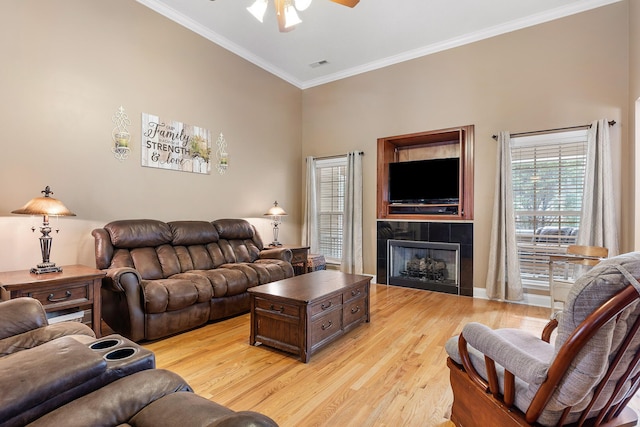 living room with ceiling fan, a tiled fireplace, ornamental molding, and light hardwood / wood-style flooring