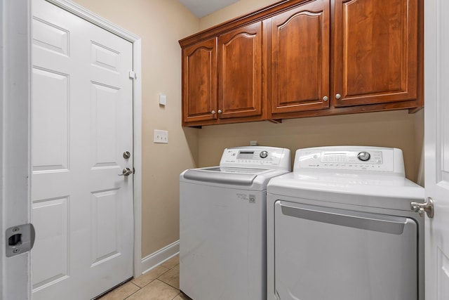 laundry area featuring washing machine and clothes dryer, light tile patterned floors, and cabinets