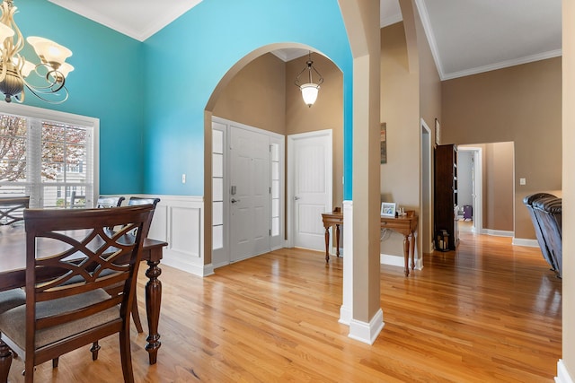 entryway with light hardwood / wood-style flooring, a towering ceiling, a notable chandelier, and ornamental molding