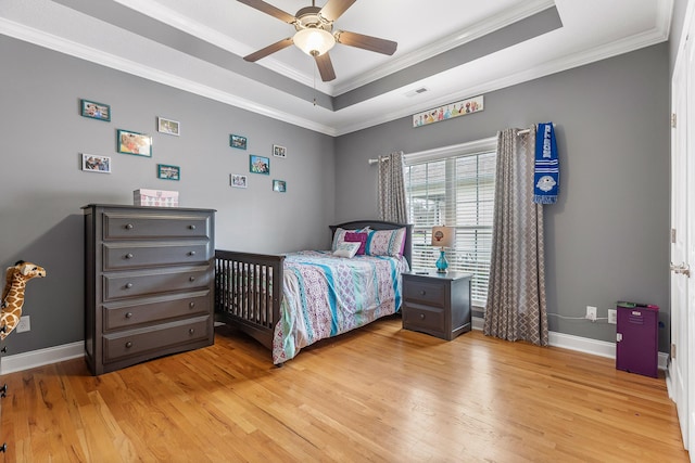 bedroom featuring a tray ceiling, ceiling fan, ornamental molding, and light hardwood / wood-style floors