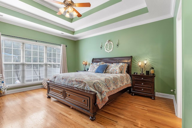 bedroom featuring a tray ceiling, light hardwood / wood-style flooring, ceiling fan, and crown molding