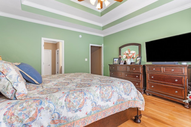 bedroom featuring ceiling fan, a raised ceiling, ornamental molding, and light wood-type flooring