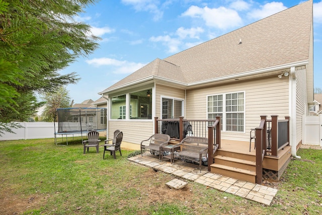 back of house with a deck, a trampoline, and a yard