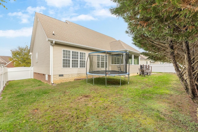 back of property with a trampoline and a yard