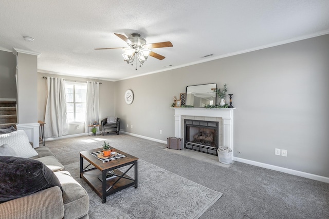 living room with a tile fireplace, crown molding, ceiling fan, a textured ceiling, and light colored carpet