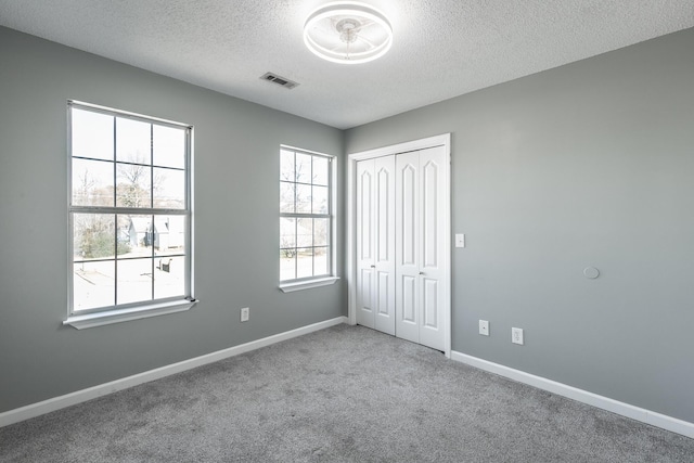 unfurnished bedroom with multiple windows, a closet, carpet, and a textured ceiling