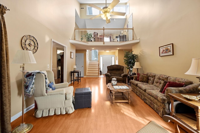 living area with baseboards, ceiling fan, stairway, and wood finished floors