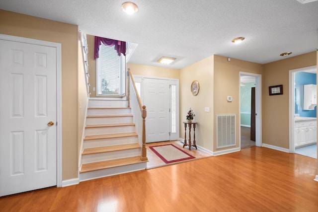 foyer entrance with stairway, a textured ceiling, visible vents, and wood finished floors