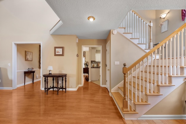 stairway featuring a textured ceiling, baseboards, and wood finished floors